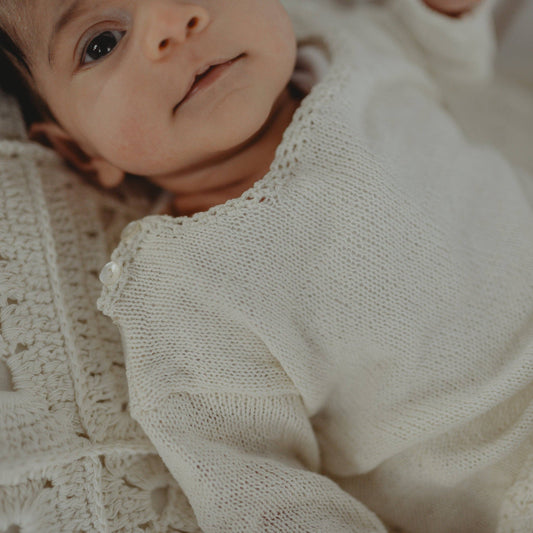 Baby in a white knitted outfit lying on a textured blanket