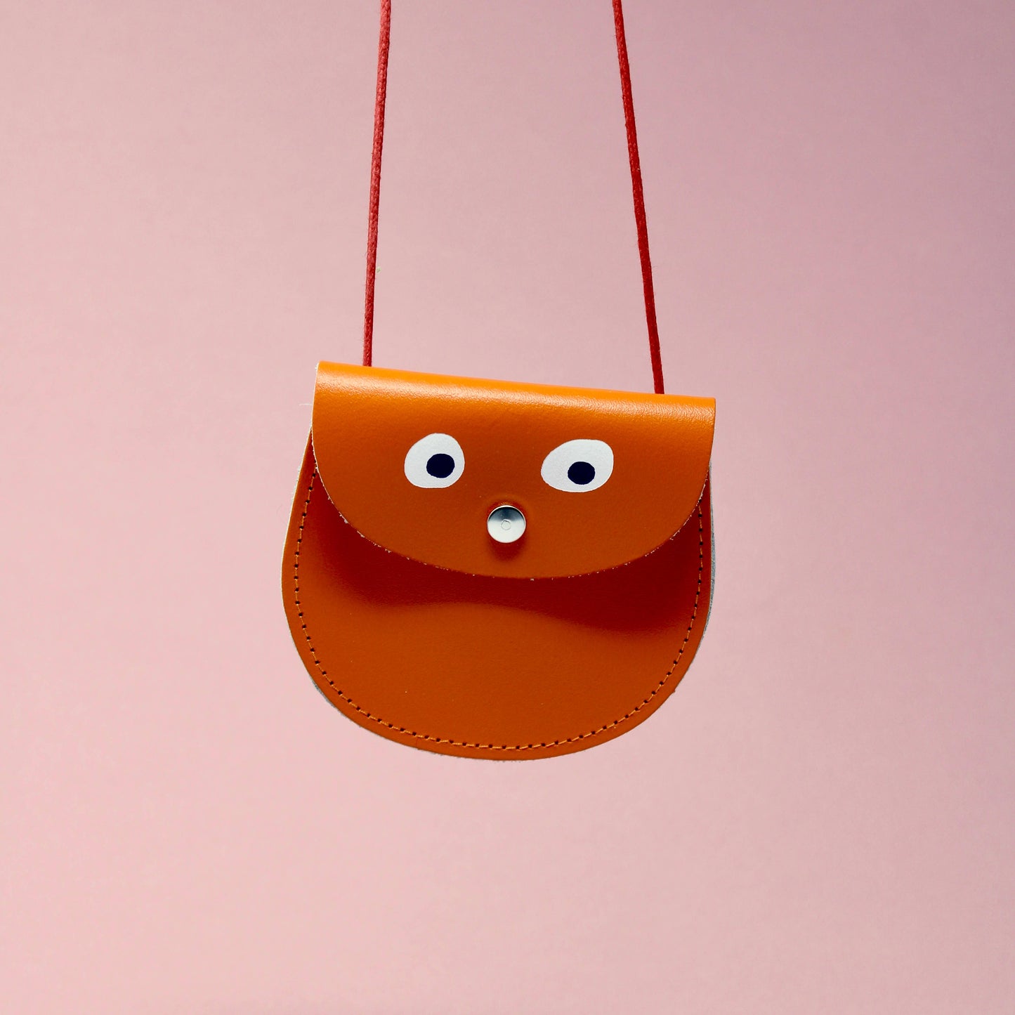 Small brown leather bag with googly eyes on a pink background