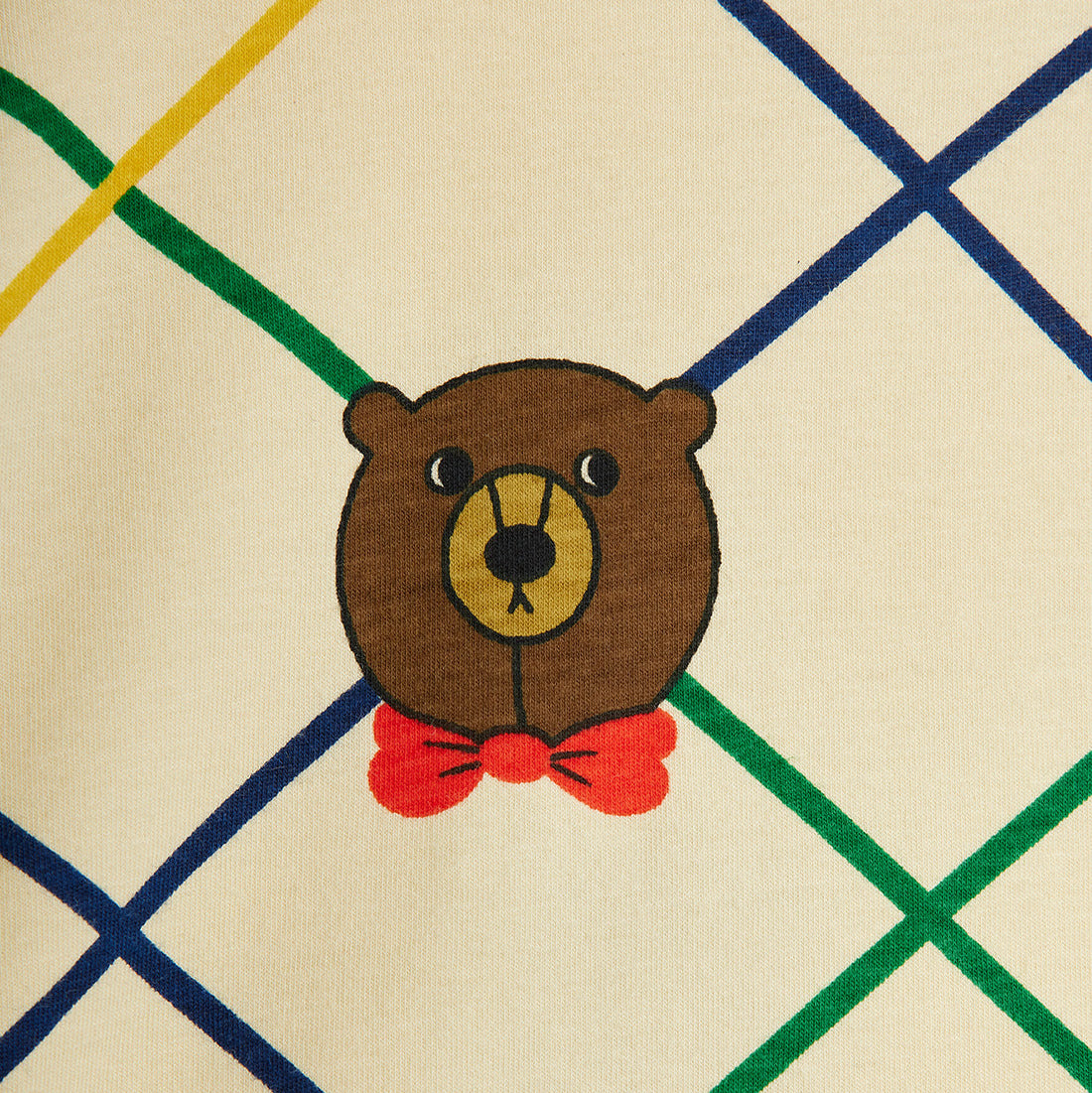 Embroidered bear face with a red bow tie on a fabric background with a diamond pattern.