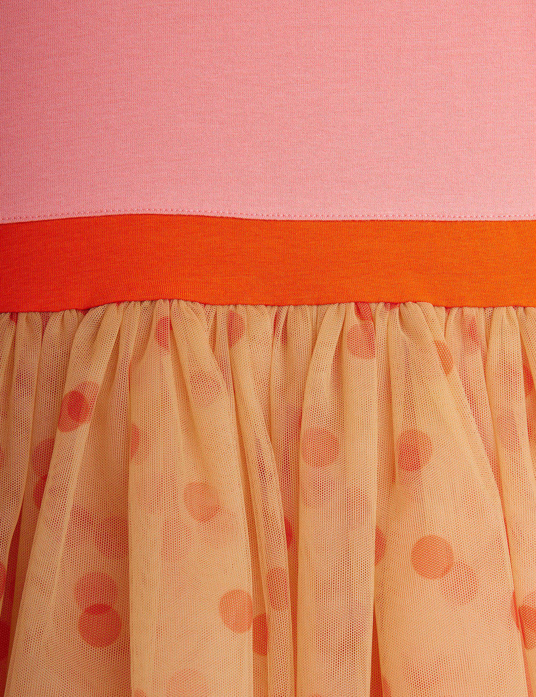 Close-up of a pink top with an orange waistband and a peach skirt with red polka dots.