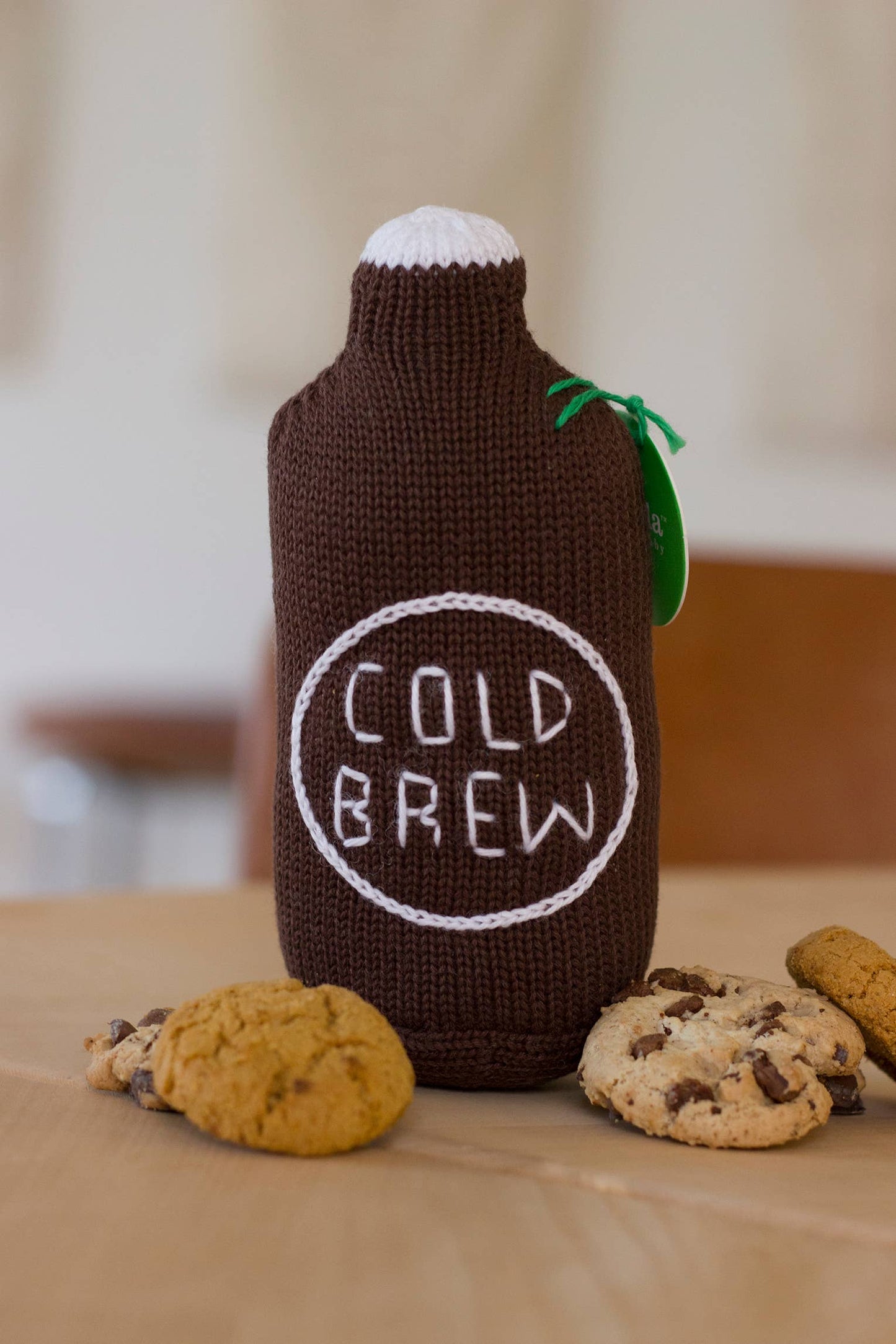 Knitted cold brew coffee bottle-shaped container with cookies on a wooden surface