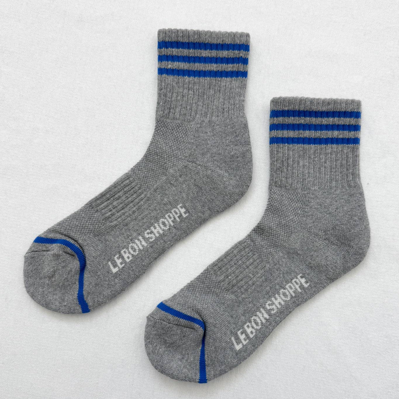 Gray socks with blue stripes and 'Le Bon Shoppe' branding on a light gray background