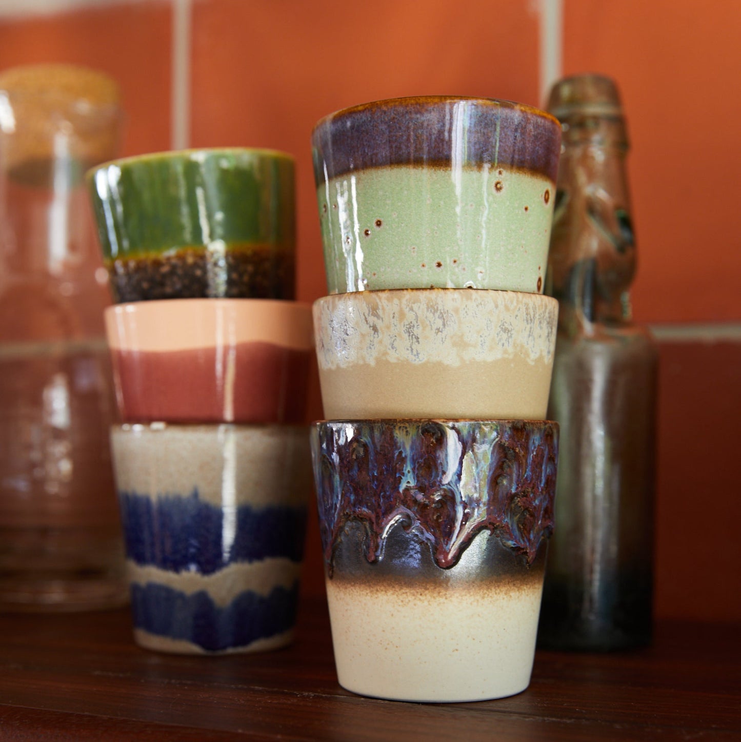 Stack of ceramic tumblers with multicolored glaze on a wooden shelf.
