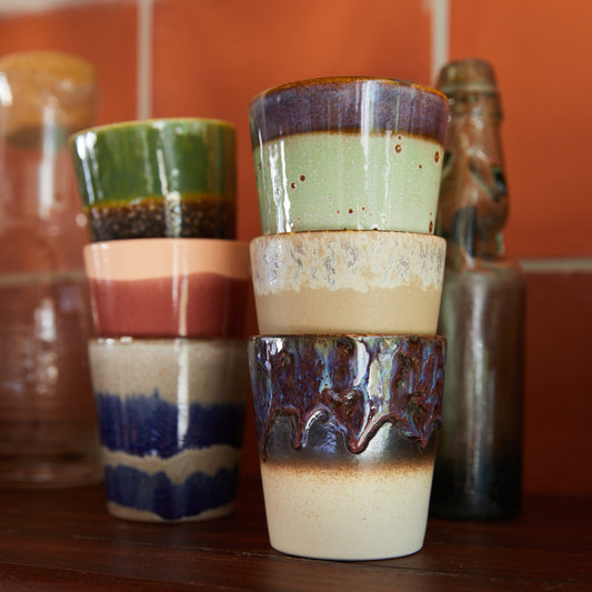 Stack of ceramic tumblers with multicolored glaze on a wooden shelf.