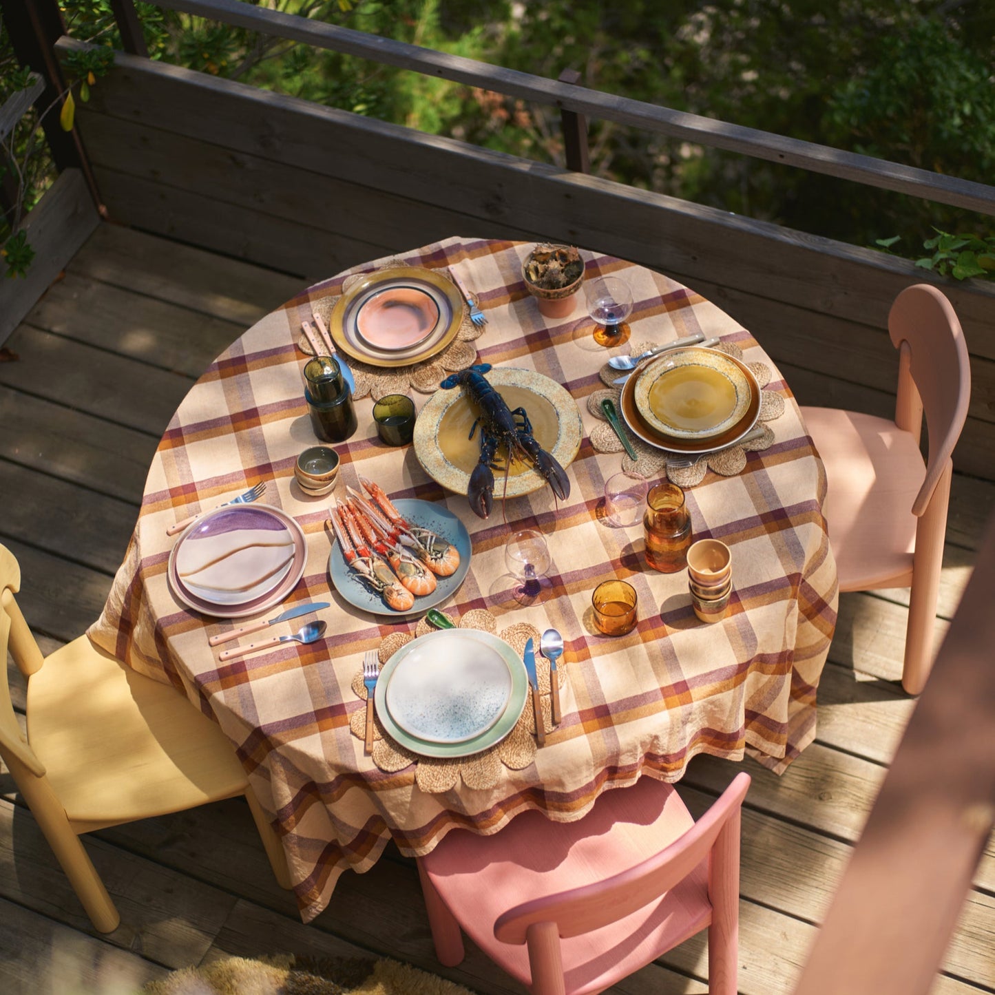 Dining table set with plates, cutlery, and glasses on a checkered tablecloth outdoors.
