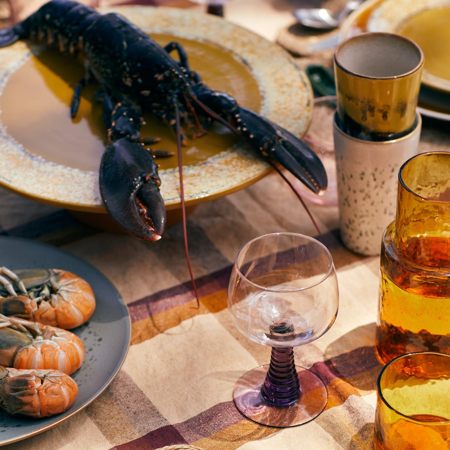 Dinner table setting with lobster, wine glasses, and colorful tablecloth.