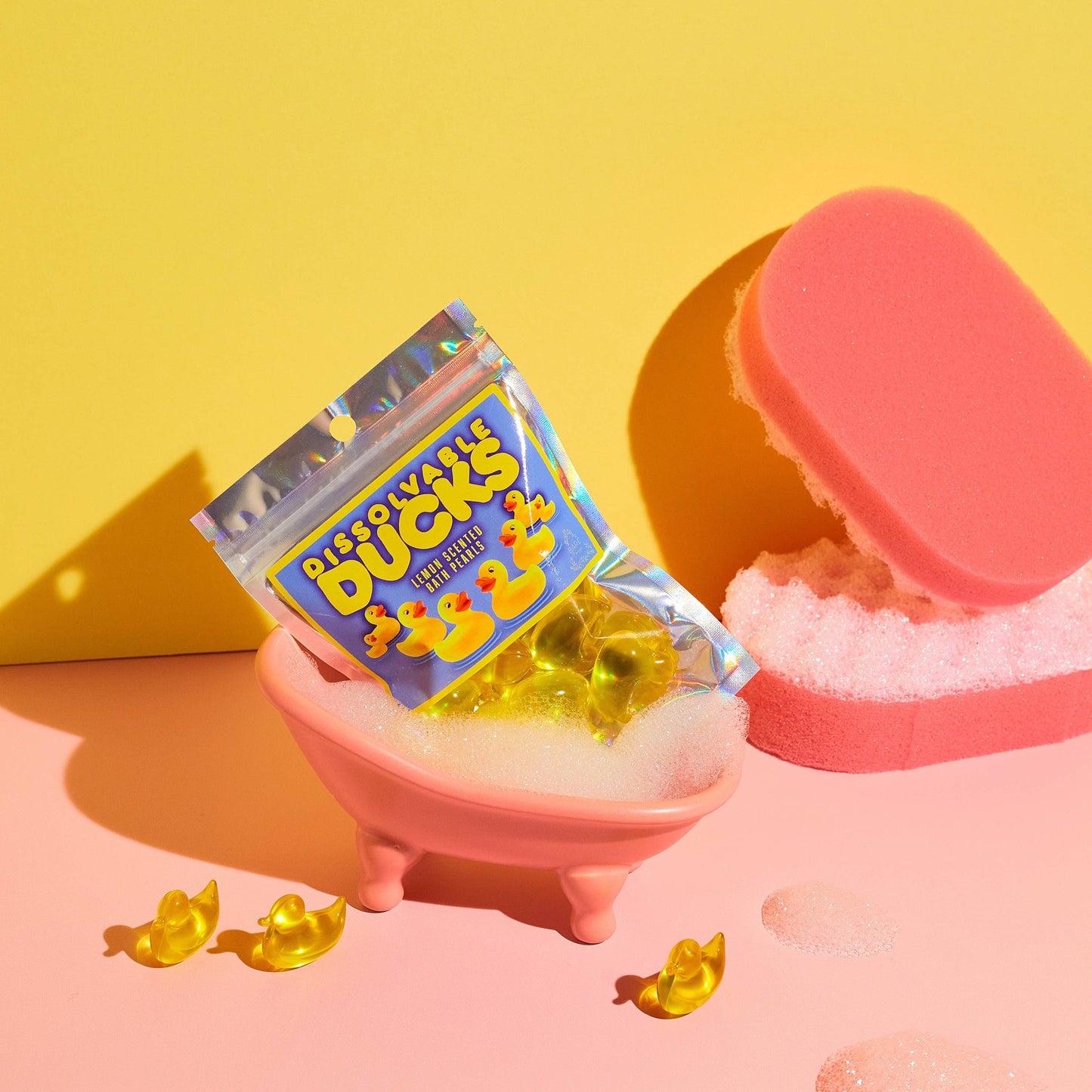 Pink toy bathtub with yellow rubber duckies and packaging on a yellow background