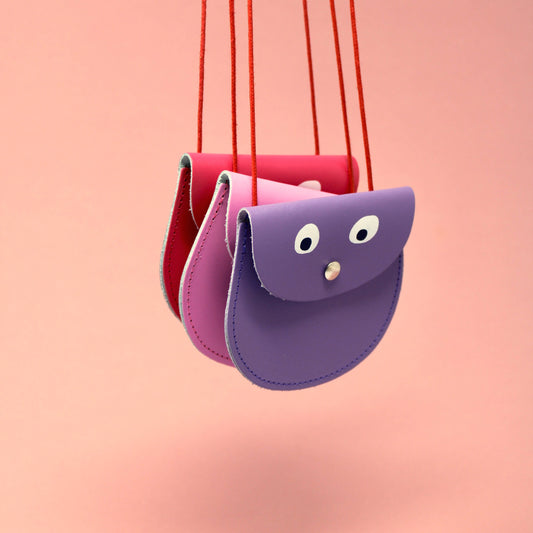 Purple and red children's bag with a face on a pink background