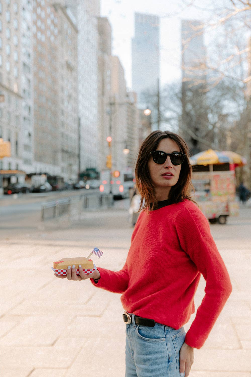 Woman in a red sweater holding a pastry on a city street