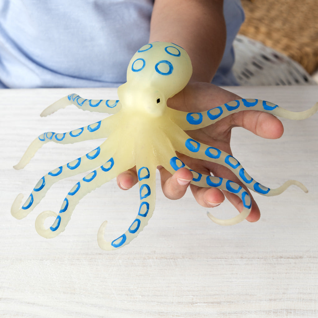 Person holding a toy octopus with blue rings on a light surface