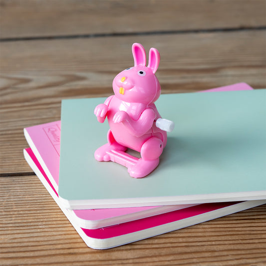 Pink cartoon-like figurine on a stack of colorful books on a wooden surface