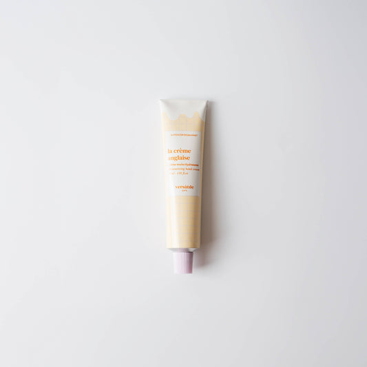 A tube of Versatile Paris hand cream with a light beige tone, lying on a white background.