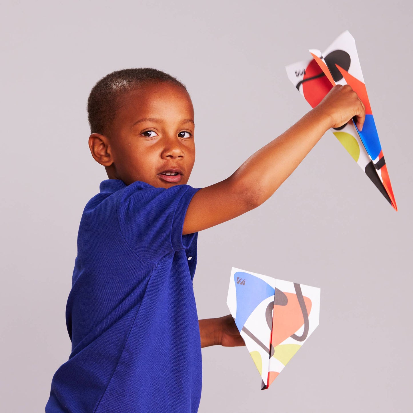 Child holding coloruful paper airplanes against a plain background