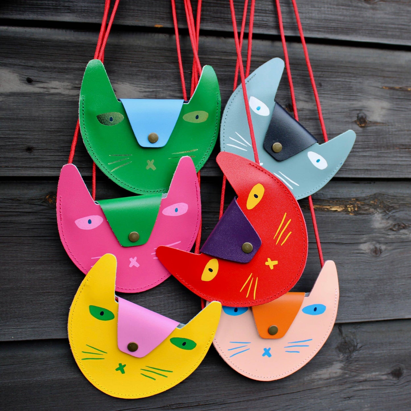 Colorful cat-shaped bags hanging against a wooden background