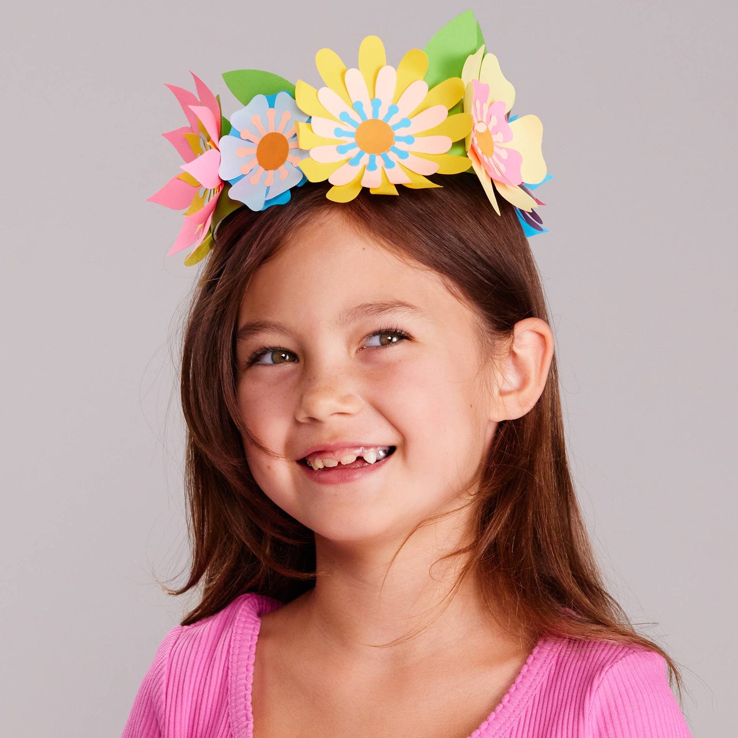 Young girl wearing a colorful flower crown against a gray background