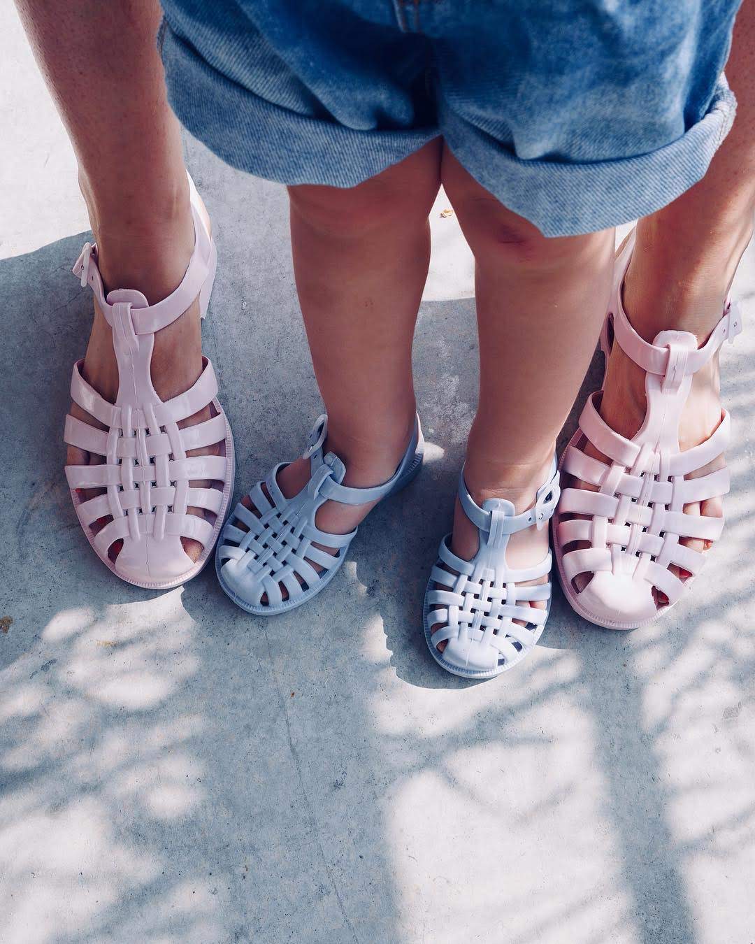 A close-up of an adult and child's feet wearing Méduse jelly sandals in pastel pink and light blue, showcasing the brand's family-friendly sizing.