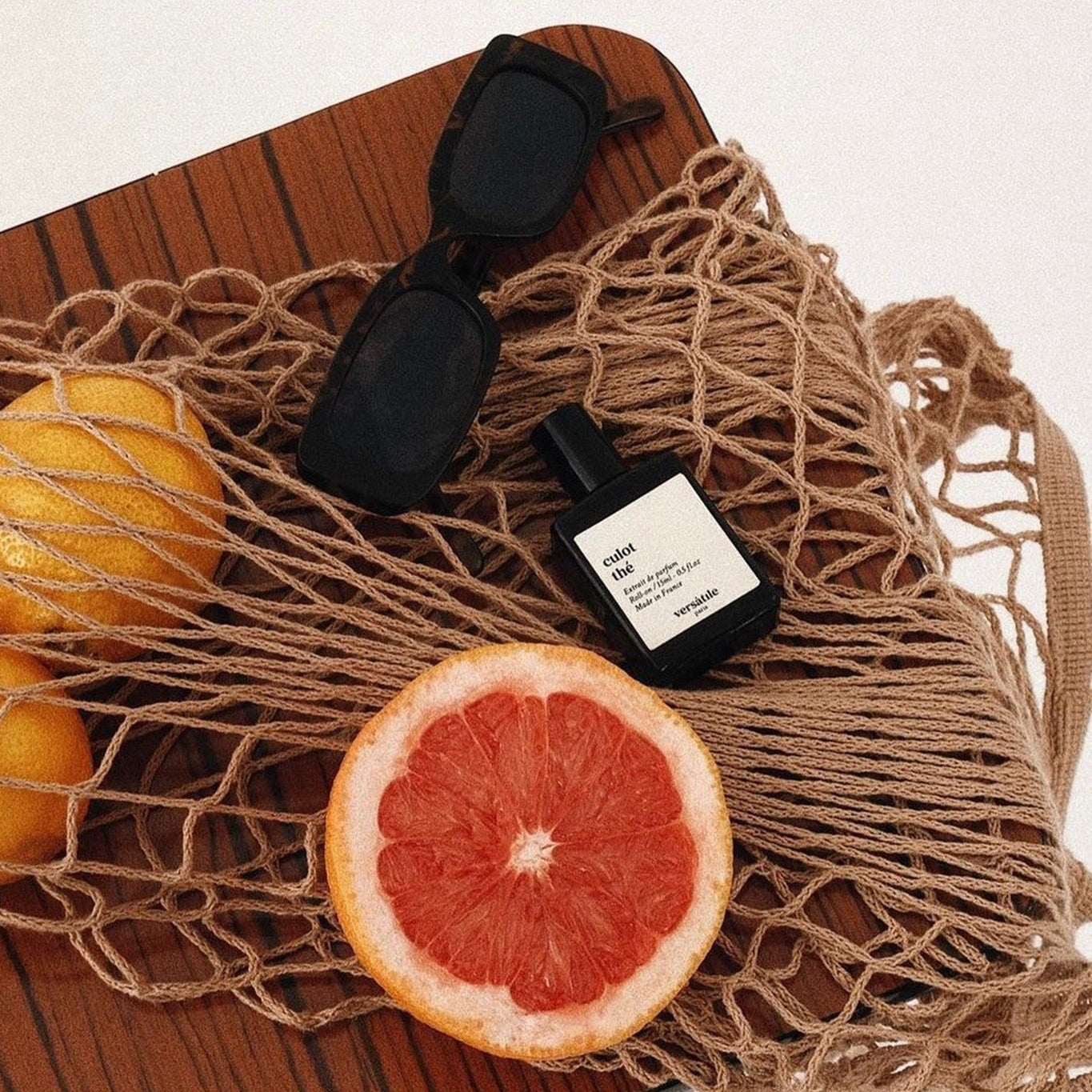 Perfume bottle, sunglasses, and grapefruit on a wooden surface with a net bag.