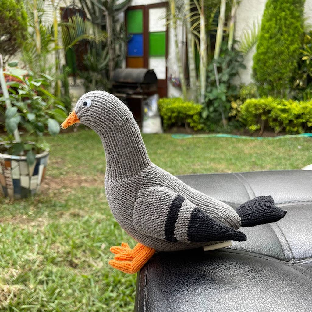 Knitted goose toy on a chair outdoors with plants in the background