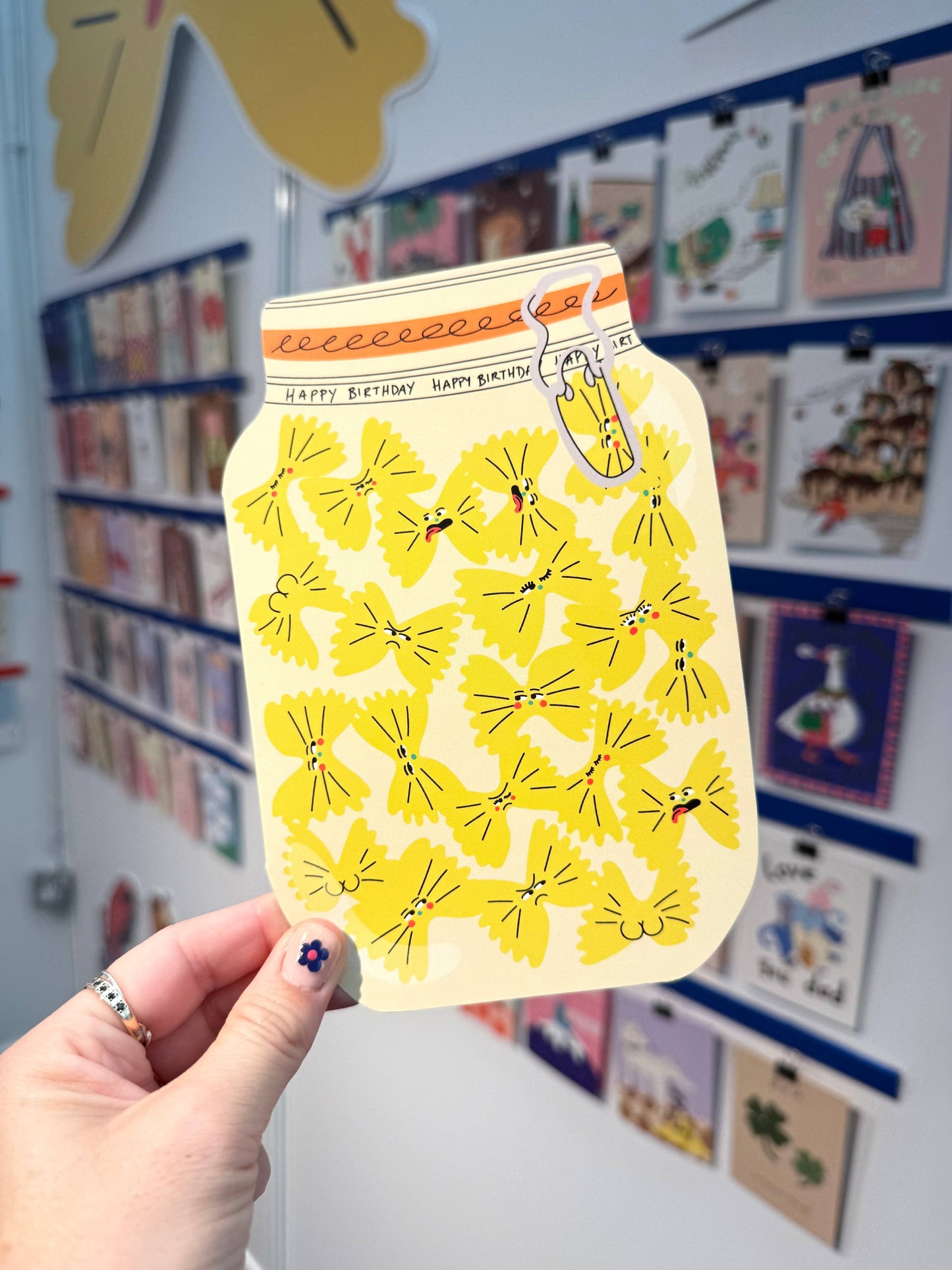 Hand holding a yellow milk carton with butterfly design against a wall with children's artwork.