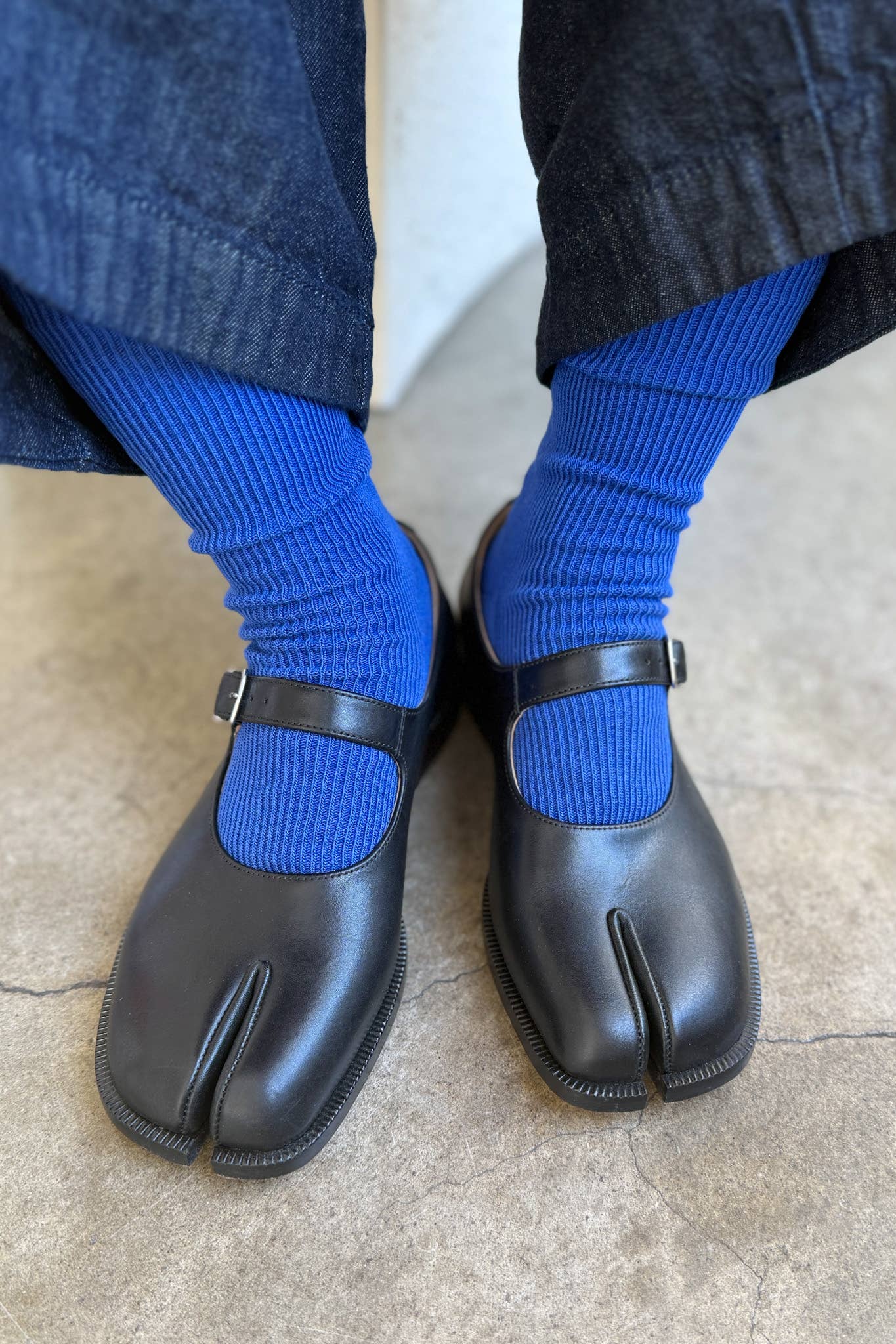 Black tabi shoes worn with blue socks on a neutral background