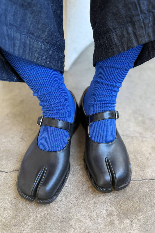 Black tabi shoes worn with blue socks on a neutral background