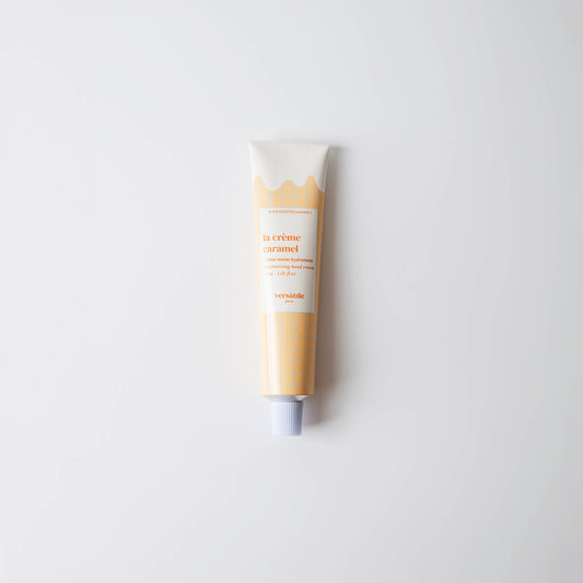 A tube of Versatile Paris Caramel Cream Hand Cream with a beige-colored body and caramel-colored label, displayed against a white background.