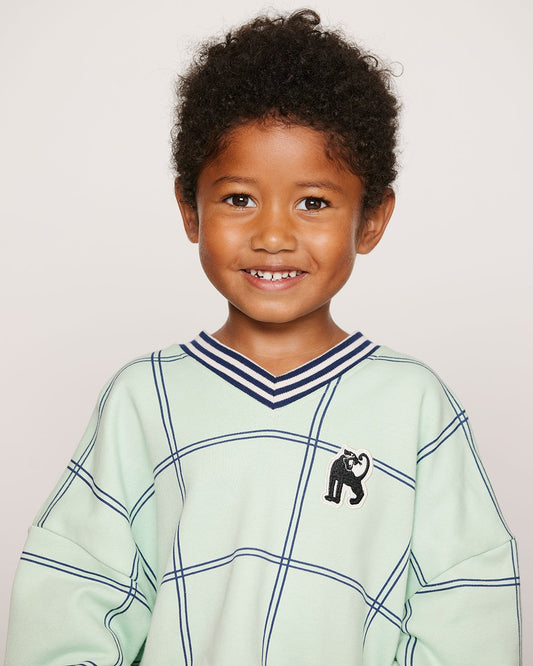 Child wearing a light green sweater with a pattern and a small logo on a plain background