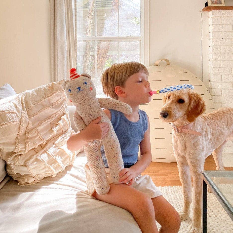 Child holding a teddy bear and blowing into a dog's nose in a cozy room.