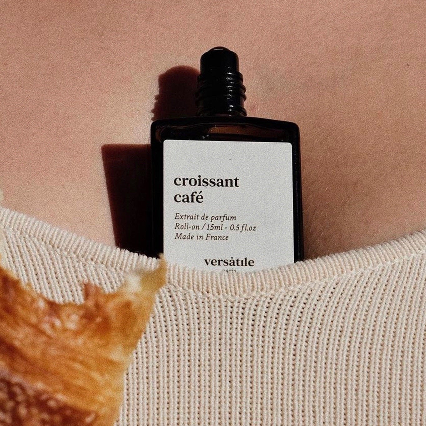 Perfume bottle labeled 'croissant cafe' by versatilie against a blurred background