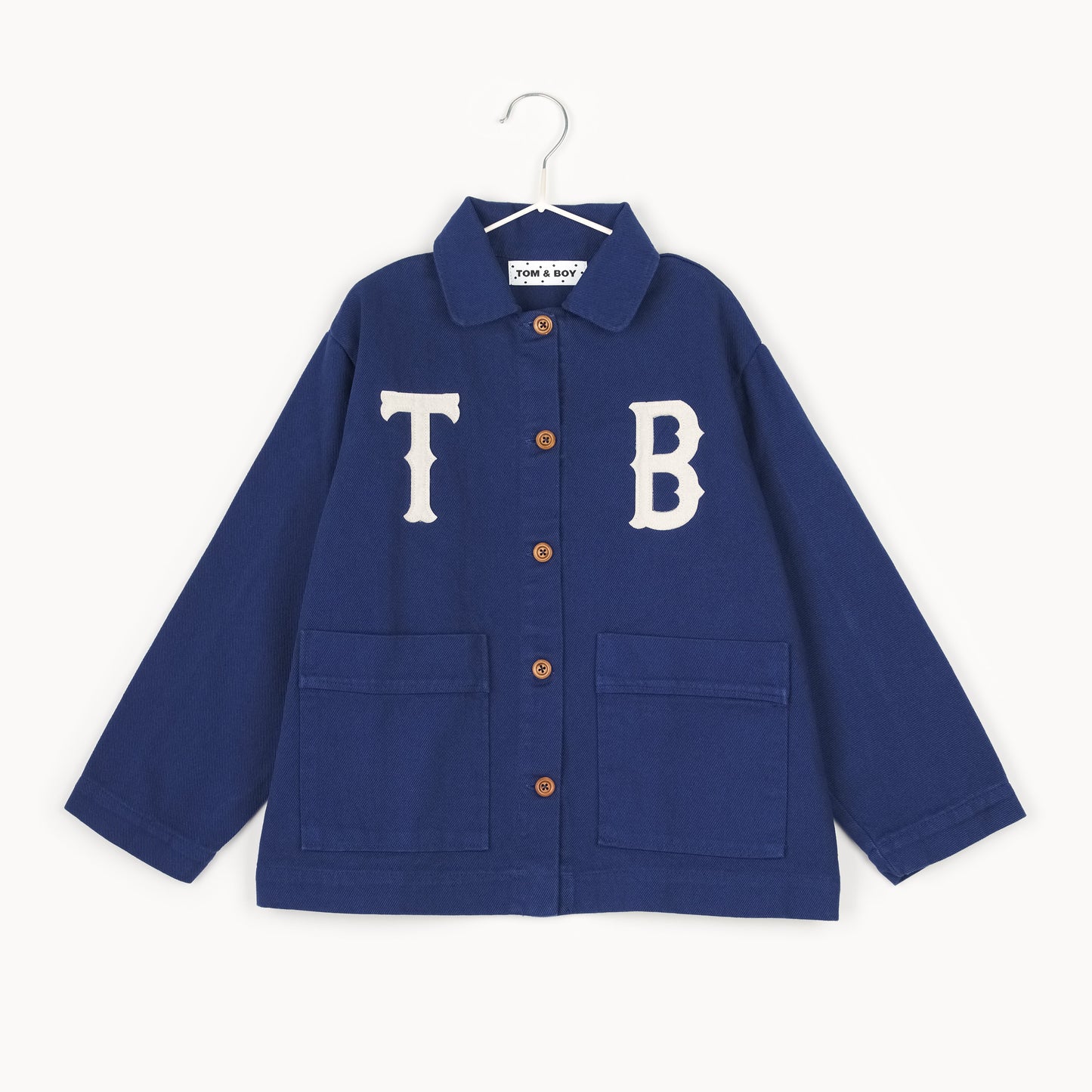 Navy kids chore jacket with oversized white appliqué letters, wooden buttons, and front patch pockets, crafted from organic cotton in Portugal.