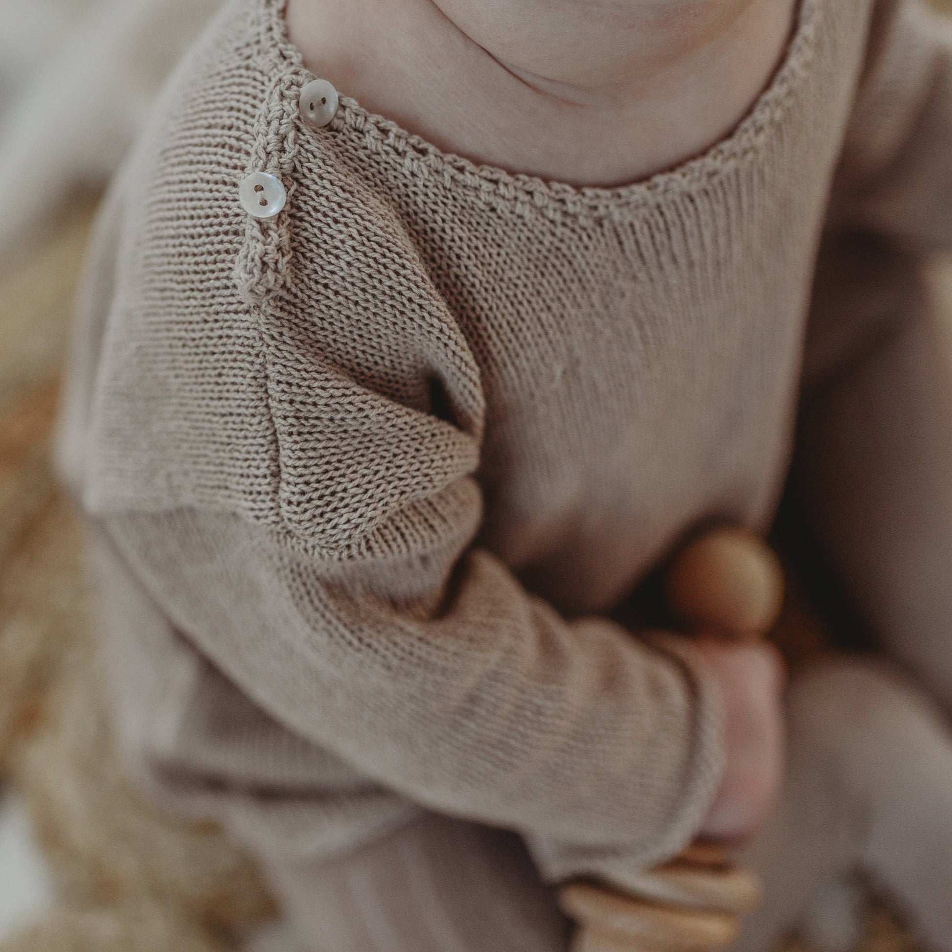 Close-up of a baby wearing a beige knitted outfit with a blurred background