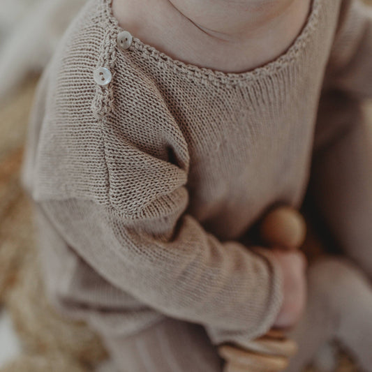 Close-up of a baby wearing a beige knitted outfit with a blurred background