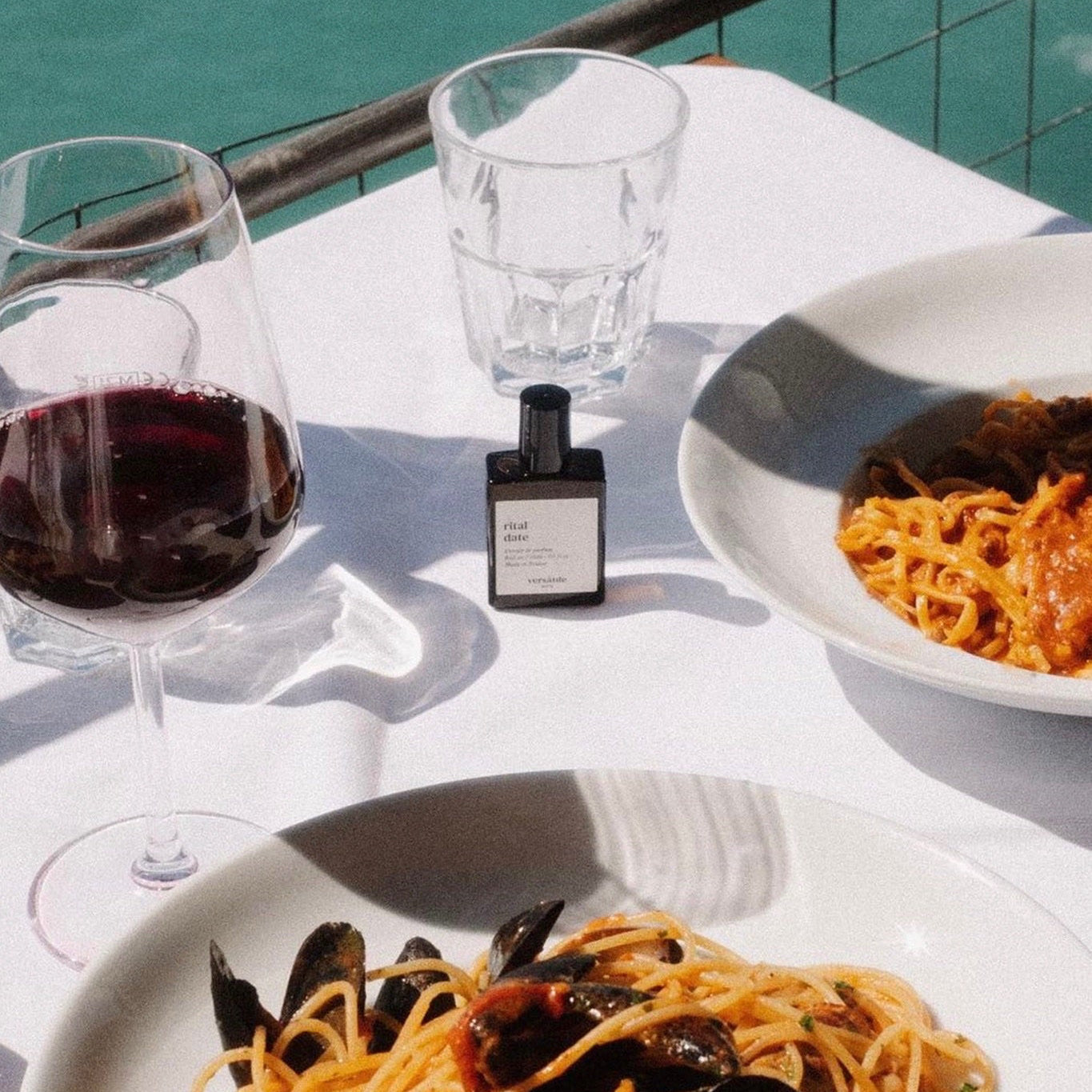Table with pasta, red wine, and a glass of water by a waterfront.