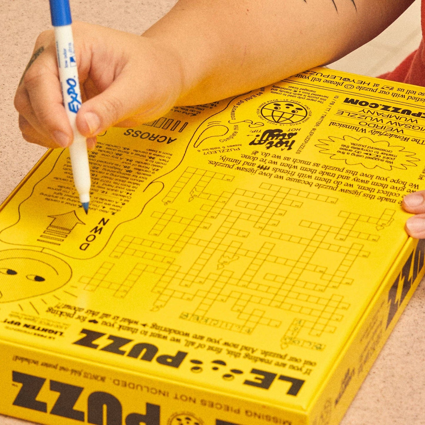 Person holding a yellow puzzle box with a pen, likely solving a crossword puzzle.