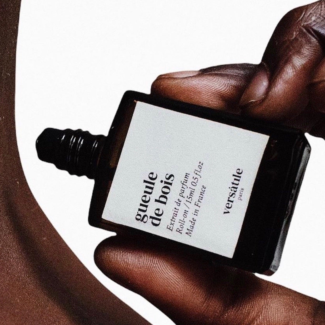 Hand holding a bottle of Versace Gueule de Bois perfume against a white background