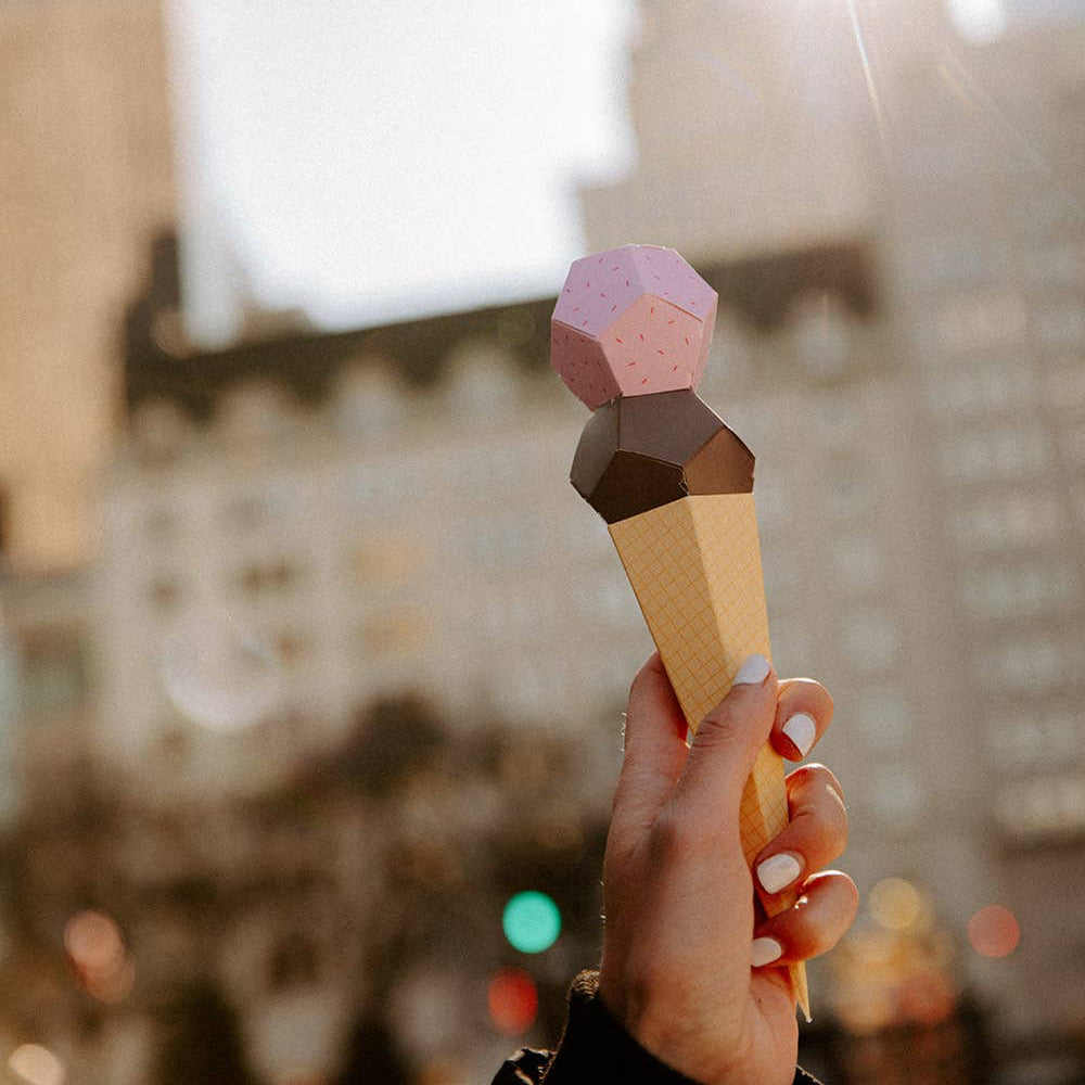 Hand holding a geometric ice cream cone toy with a cityscape in the background