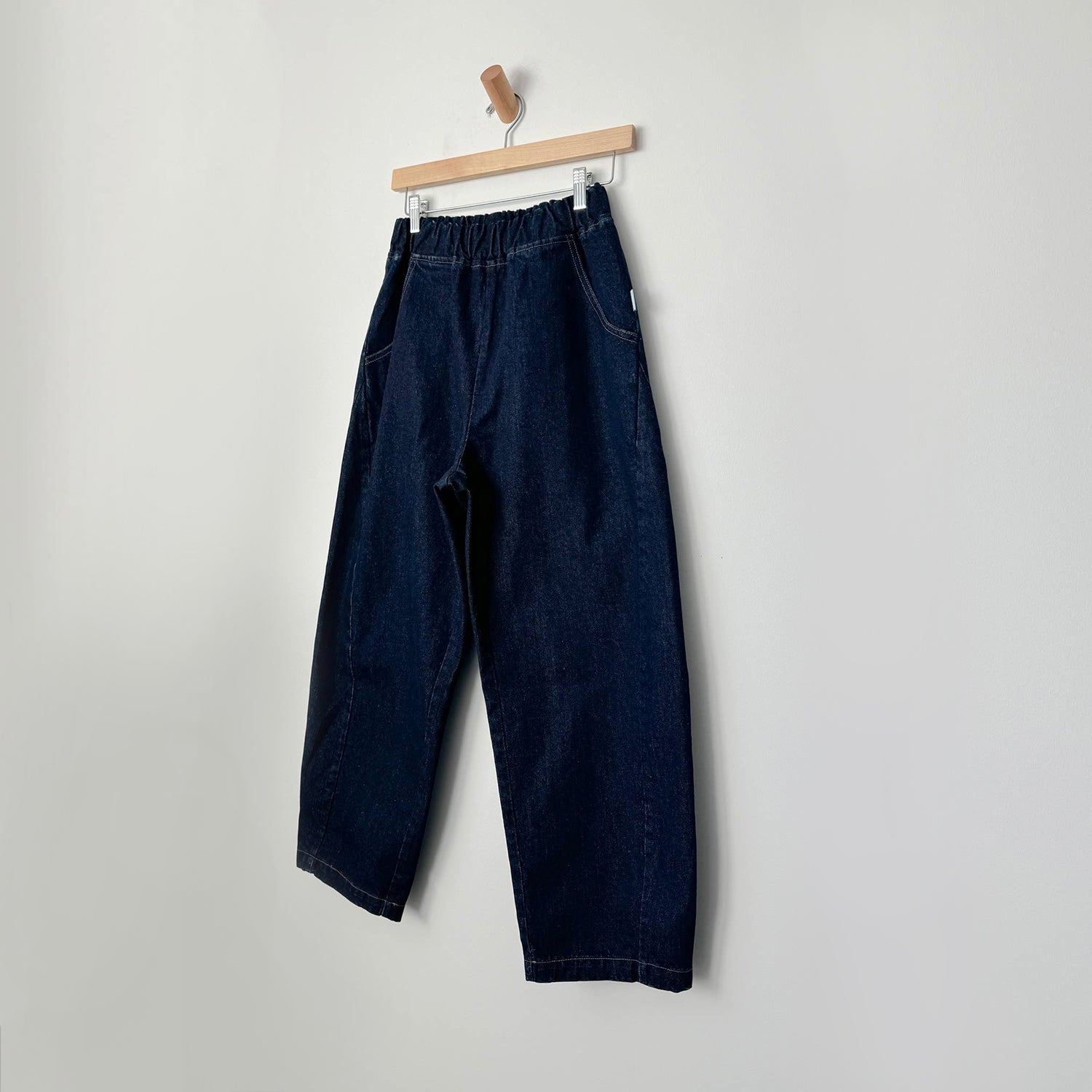 Relaxed wide-leg jeans with an elasticated waist and contrast stitching, displayed on a wooden hanger against a neutral background.