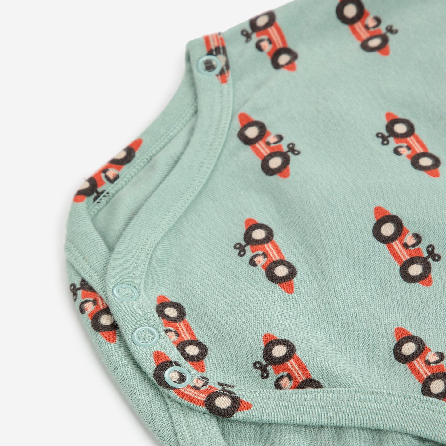Green baby onesie with red tractor pattern on a white background