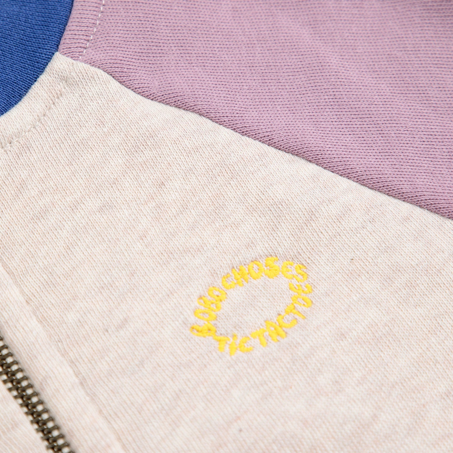 Close-up of a jacket with colour-blocked sleeves and a yellow embroidered design on a white background.