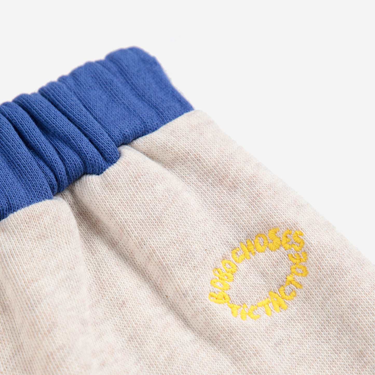 Close-up of a beige sweatshirt with blue cuffs and a yellow embroidered logo on a white background