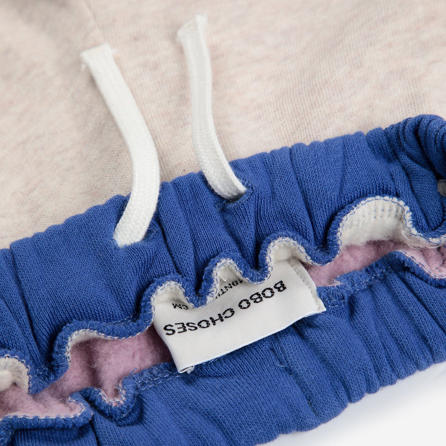 Close-up of blue baby romper with pink trim and 'Bogo Choses' label on a beige background