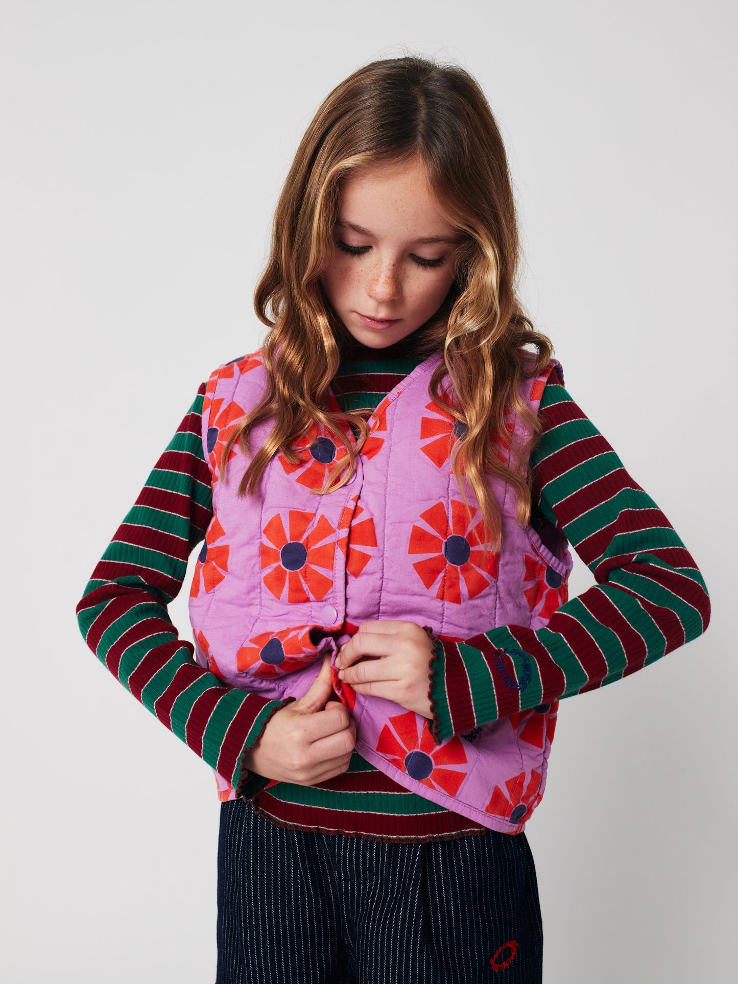 Young girl wearing a colorful quilted vest with a white background