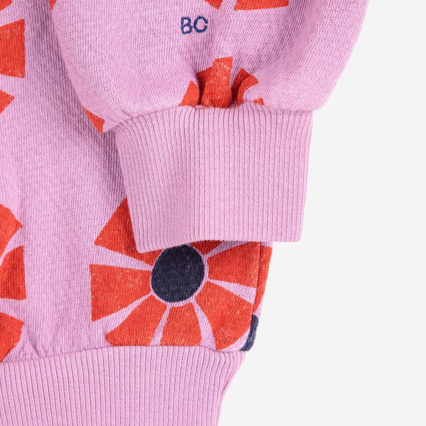 Close-up of a pink sweater with red floral patterns on a white background