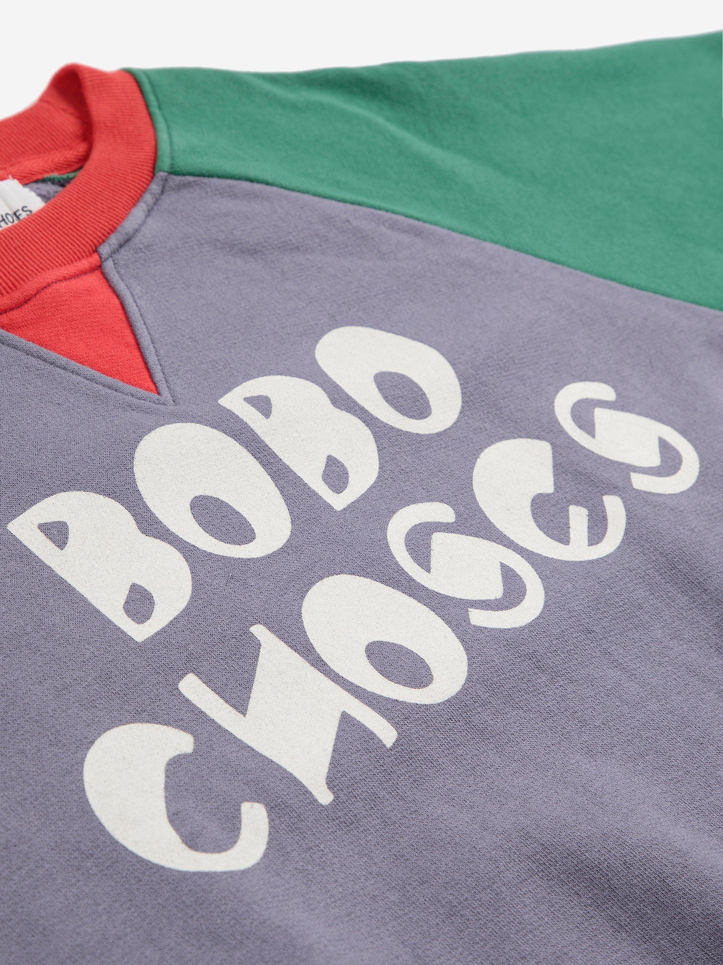 Close-up of a gray sweatshirt with 'BOBO CHOSES' text, red and green sleeves on a white background.
