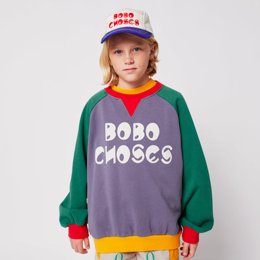 Child wearing a colorful sweater and cap with 'BOBO CHOSES' branding on a light gray background