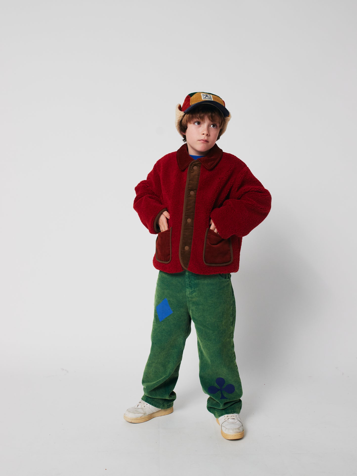 Child wearing a red jacket and green pants on a white background