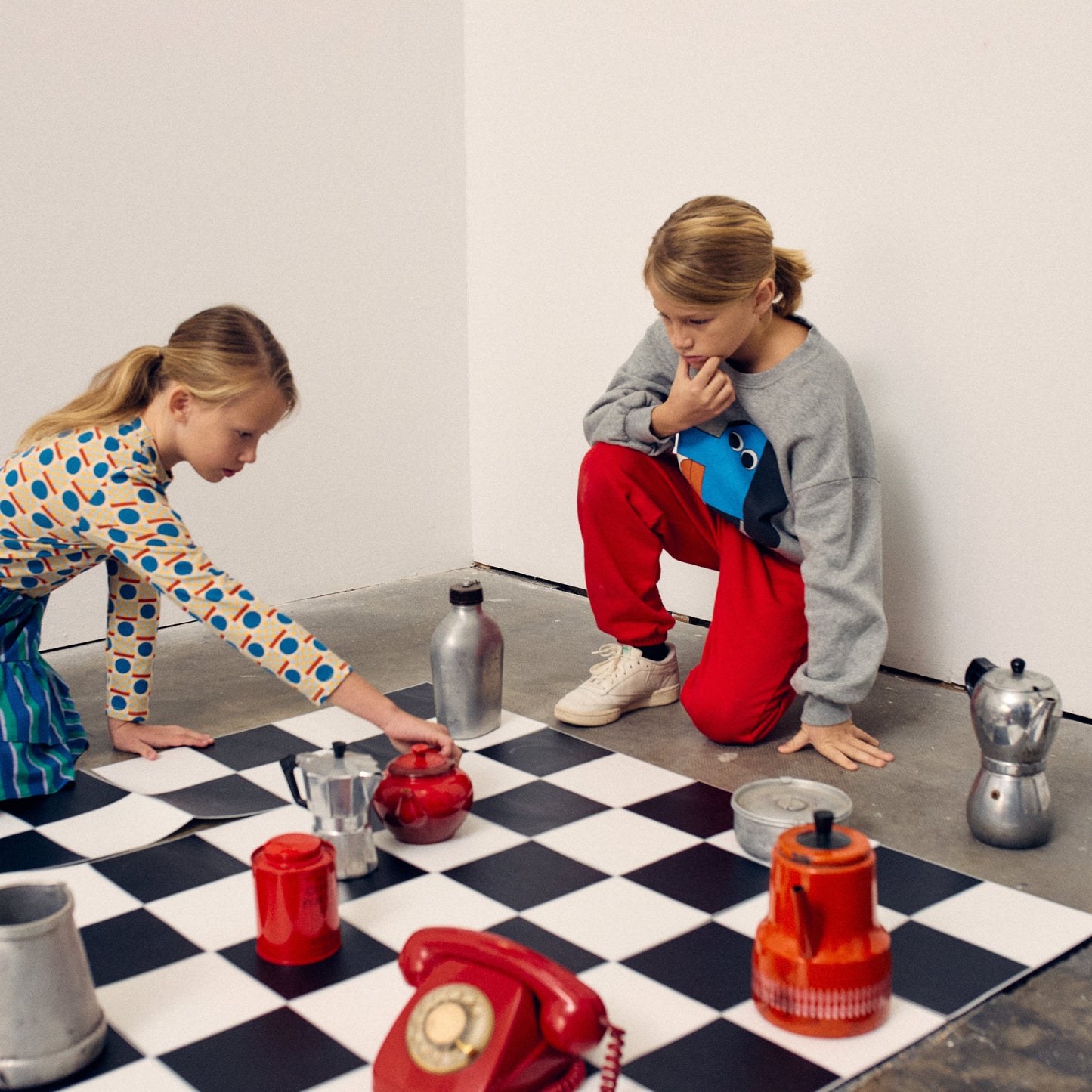Two children playing with toy kitchen items on a checkered floor.