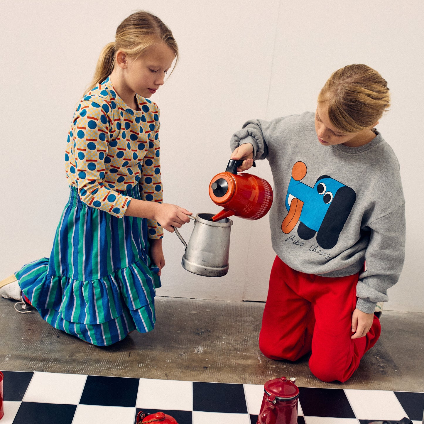 Two children playing with colorful bottles on a checkered floor.