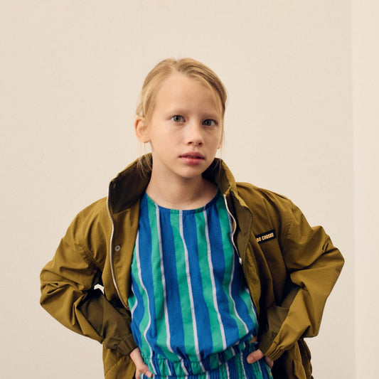 Child wearing a green jacket over a blue striped shirt against a plain background