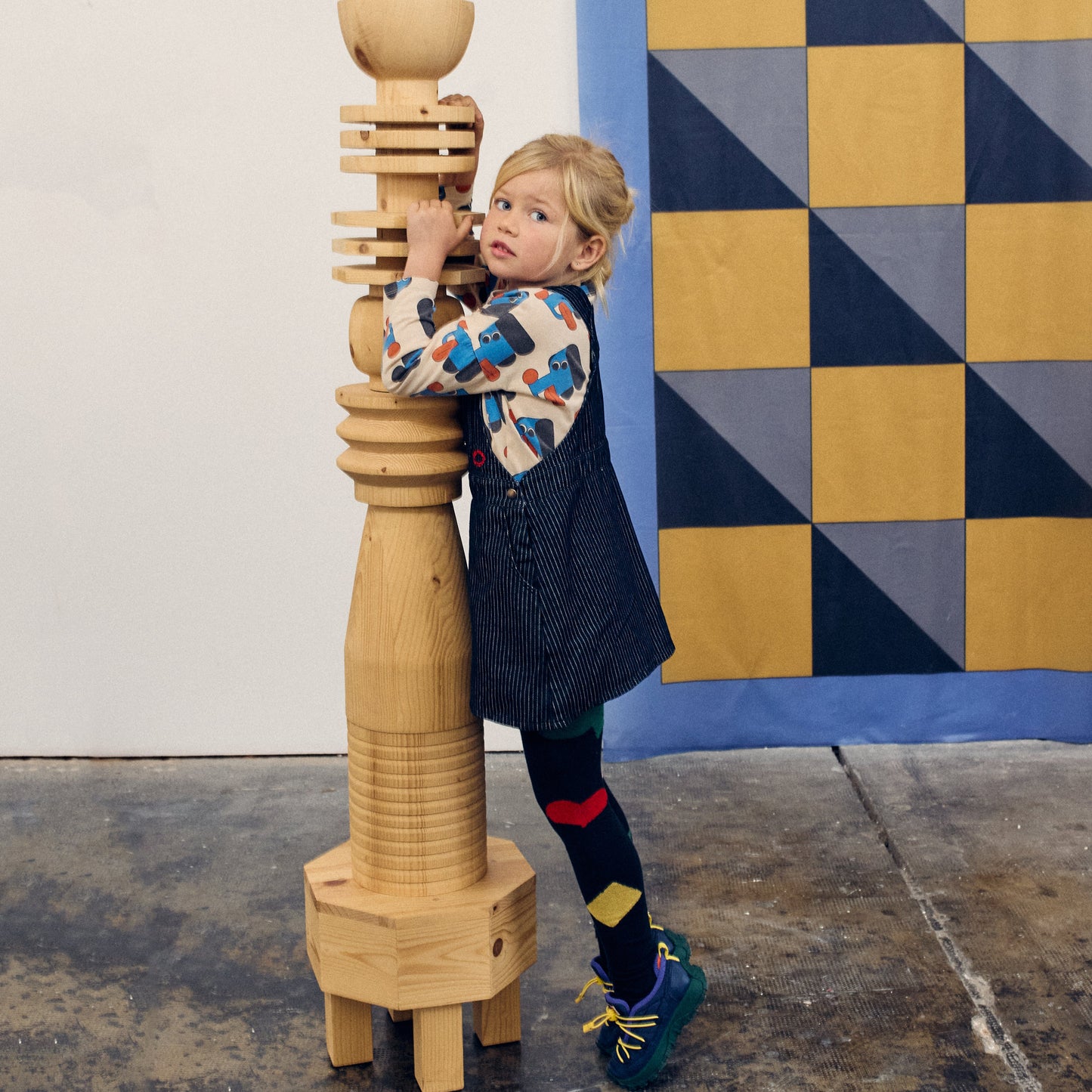 Child playing with a wooden sculpture against a geometric-patterned wall.